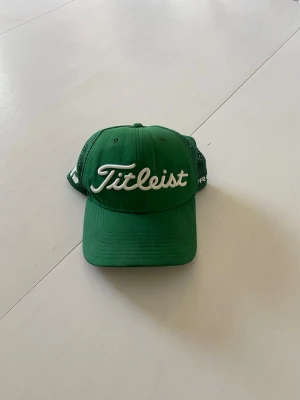 Grön Titleist keps med mesh - Snygg grön keps från Titleist med vit broderad logga framtill. Kepsen har böjd skärm och mesh-paneler på sidorna och bak för extra ventilation. Justerbar snapback baktill för perfekt passform. Perfekt för golfbanan eller vardagslooken.