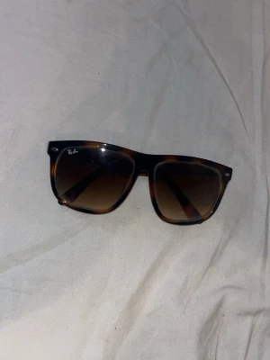 Bruna solglasögon Ray-Ban - Säljer nu dessa populära solglasögon från Ray-Ban med brunmelerad båge och mörka glas. Klassisk form som passar till de flesta stilar. Perfekta för soliga dagar och ger en cool vibe.