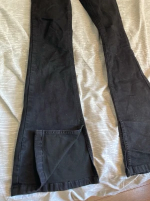 Svarta utsvängda jeans - Säljer ett par svarta jeans med utsvängda ben och hög midja. Jeansen har en klassisk femficksmodell och är tillverkade i ett stretchigt bomullsmaterial som sitter snyggt. Perfekta för dig som gillar retrostil och vill ha ett par bekväma och trendiga jeans. Storlek 36!