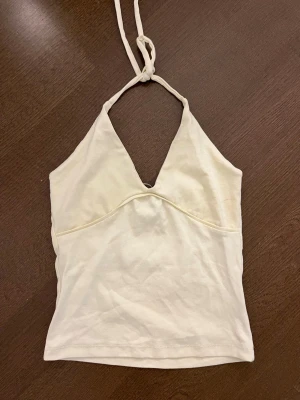 Vit halterneck linnetopp - Snygg vit linnetopp med halterneck och v-ringad front. Toppen har knyt i nacken och är ärmlös, perfekt för varma dagar. Tillverkad i mjukt bomullsmaterial och har en enkel, clean look som passar till det mesta.