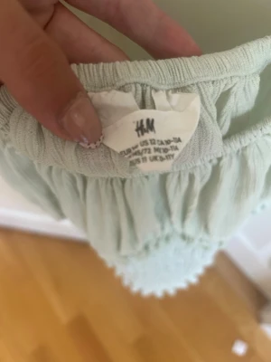 Ljusgrön smockad topp från H&M - Supersöt ljusgrön topp från H&M med smockad midja och kort puffärm. Toppen har en bred, rundad urringning och är tillverkad i ett tunt, mjukt tyg som känns luftigt. Perfekt till jeans eller kjol för en fräsch look.