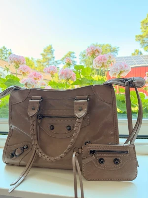 Beige handväska med flätat handtag - Snygg beige citybag liknande väska med flätade handtag och silvriga detaljer. En väldigt rymlig väska som har två fack på insidan och även ett på utsidan. Korthållare medföljer! Köpt på en marknad på Öland. Endast använd fåtal gånger 💕