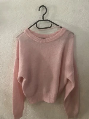 Ljusrosa stickad tröja Vero Moda - Mysig ljusrosa stickad tröja från Vero Moda med rund halsringning och långa ärmar. Tröjan har en fluffig och mjuk känsla, ribbstickade muddar vid ärmslut och nederkant. Perfekt för lager-på-lager och chill dagar.
