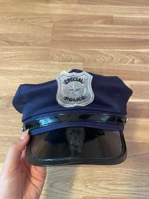 Mörkblå polis-hatt - Mörkblå polis hatt med silverfärgad polisbricka framtill där det står 'Special Police'. Skärmen är i svart, glansigt material och hatten är gjord i tyg. Perfekt för maskerad eller cosplay som polis.