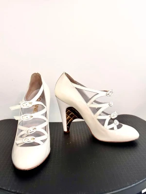 Chanel skor! Vita pumps med remmar och guldklack - Unika vita pumps med flera smala remmar och spännen framtill. Skorna har hög klack med gulddetaljer i quiltat mönster på insidan. Tillverkade i glansigt material som ger en lyxig känsla och modern look.