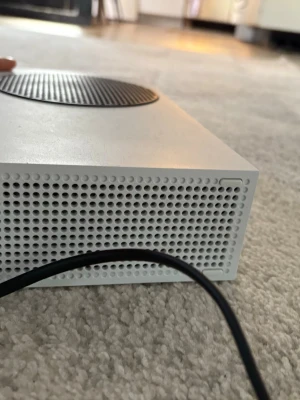 Vit Xbox Series S spelkonsol, Utan kontroll  - Säljer en vit Xbox Series S spelkonsol med stilren, kompakt design och rund svart ventilationsyta på ovansidan. Konsolen har flera portar på baksidan för HDMI, USB och nätverk. Perfekt för gaming med modern prestanda.