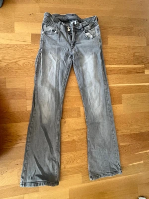 Grå bootcut jeans med dubbla knappar - Säljer ett par grå bootcut jeans med dubbla knappar i midjan och klassiska fem fickor. Jeansen har en lätt tvättad look och raka ben. Perfekta för dig som gillar en avslappnad men ändå stilren vibe.