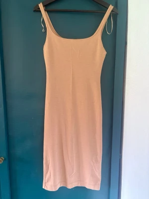 Zara Beige ärmlös midiklänning S  - Säljer en enkel och stilren beige klänning med smala axelband och rak passform. Klänningen är ärmlös och har en liten slits bak för extra rörelsefrihet. Perfekt för varma dagar eller att styla med en skjorta över.