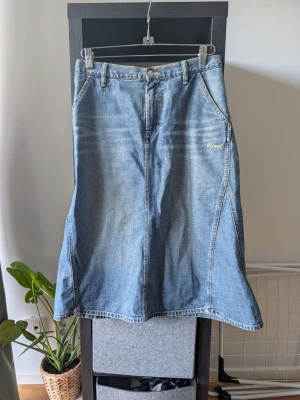 Lång jeanskjol med fickor - Säljer en klassisk blå lång jeanskjol med fickor fram och bak samt bälteshällor. Kjolen har en lätt utsvängd form och sömdetaljer som ger en snygg siluett. Perfekt för dig som gillar denim och vill ha en tidlös stil.
