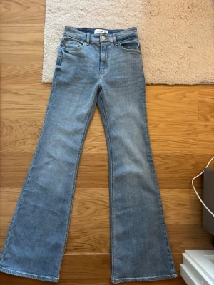 Ljusblå tall bootcut jeans med hög midja - Säljer ett par ljusblå tall bootcut jeans med hög midja och klassisk femficksmodell. Jeansen har utsvängda ben och är tillverkade i mjuk denim. Andvädna endast en gång så super bra skick. 