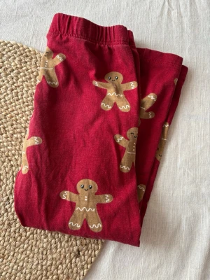 Röda leggings med pepparkaksgubbar - Snygga röda leggings med gulligt pepparkaksgubbemönster. Mjukt och stretchigt material med resår i midjan för skön passform. Storlek 104 