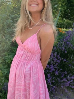 Rosa långklänning med zebramönster - Säljer en söt rosa långklänning med vitt zebramönster. Klänningen har smala axelband, v-ringad urringning och ett luftigt fall. Perfekt för varma dagar och ger en fräsch sommarkänsla.