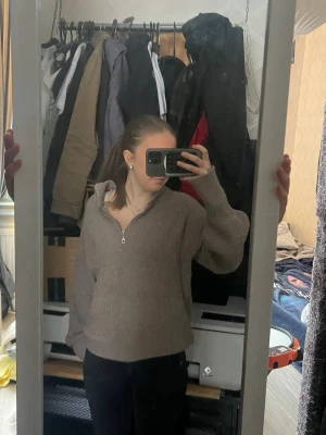 Beige stickad tröja med dragkedja - Mysig brun stickad tröja med halv dragkedja framtill och hög krage. Tröjan har en avslappnad passform och långa ärmar med breda muddar. Perfekt för lager på lager och enkel att matcha till olika outfits.