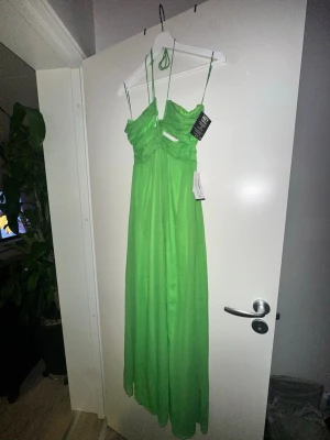 Grön långklänning med tunna band - Snygg grön långklänning med tunna axelband och draperad överdel. Klänningen har en luftig och flowy passform, perfekt för sommarens alla tillfällen. Tillverkad i ett lätt och glansigt material som ger en elegant känsla.