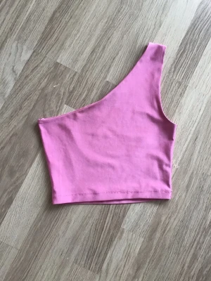 Rosa oneshoulder top från BokBok, stl XS - Rosa top med asymmetrisk one shoulder-design. Storlek XS. Har en likadan i svart också. Just nu fri frakt, så du betalar bara för toppen. Jag har fler plagg ute, och hittar du något mer från min garderobsutrensning, så skickar jag i samma paket.