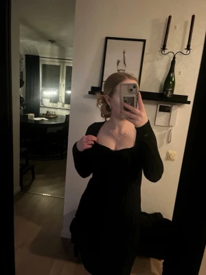 Svart ribbad klänning med lång ärm - Säljer en svart klänning med ribbad struktur och lång ärm. Klänningen har en djup, rundad urringning och sitter figurnära. Perfekt för dig som gillar en enkel men snygg look. Materialet ser ut att vara stretchigt och bekvämt.