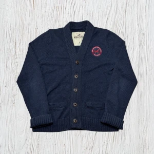 Vintage Hollister grovstickad kofta - herr strl L (M) - Säljer en Vintage Hollister grovstickad kofta i marinblå färg i storlek L, passar som M, med Hollister bird brodering på bröstkorgen.  👕 Märke: Hollister 📏 Storlek: L, passar som M 🎨 Färg: Marinblå 🧵 Material: 85% bomull, 15% akryl 📐 Mått: 64 cm lång, 50 cm bred 📌 Skick: Mycket bra skick (se bilder)  💬 Hör av dig vid frågor 💰 Pris kan diskuteras vid snabb affär 📦 Skickas inom 24 timmar