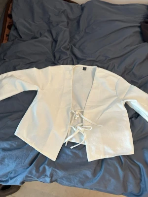 Vit kimono jacka cosplay - Säljer en vit kimono-inspirerad jacka perfekt för cosplay eller maskerad. Jackan har långa ärmar och knyts med två band framtill. Materialet är ett lätt tyg som ger en autentisk känsla till din outfit.