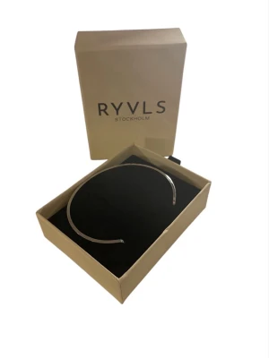 Silverfärgat armband från RYVLS - Snyggt och stilrent armband från RYVLS Stockholm i silverfärgad metall. Armbandet har en minimalistisk och öppen design som gör det enkelt att matcha med andra accessoarer. Levereras i original ask.
