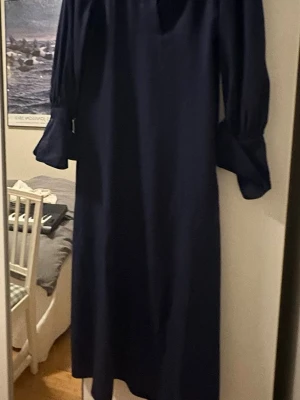GANT, Marinblå långklänning med krage - Säljer min stilren marinblå långklänning från Gant med klassisk krage och v-ringad hals. Klänningen har långa ärmar med breda manschetter och knappar. Materialet känns mjukt och har ett elegant fall, perfekt för dig som gillar en tidlös look.