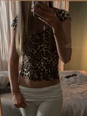 Leopardmönstrad croppad topp - Säljer en croppad topp med leopardmönster och korta ärmar. Toppens färg går i beige och svart och har en snygg v-ringning. Perfekt för dig som gillar att sticka ut och vill ha något trendigt i garderoben. Xs/s