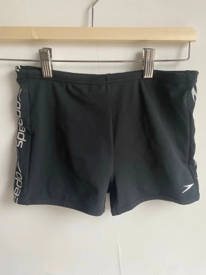 Svarta badbyxor från Speedo - Säljer ett par svarta badbyxor från Speedo med logga på vänster ben och vit Speedo-text längs sidan. Klassisk tight passform och elastisk midja. Perfekta för simträning eller strandhäng. Materialet är snabbtorkande och bekvämt.