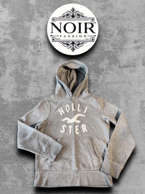 Grå hoodie från Hollister - Snygg grå hoodie från Hollister med stor vit logga och text på bröstet. Klassisk känguruficka framtill och justerbar huva med snörning. Mjuk bomullsblandning som känns skön mot huden. Perfekt för en avslappnad och trendig look.