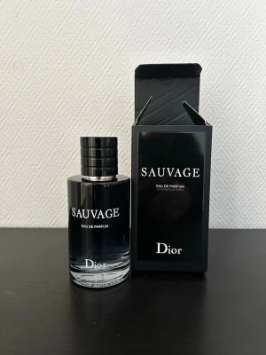 Dior Sauvage Eau de Parfum - Dior Sauvage Eau de Parfum är en elegant herrdoft i en stilren, mörk glasflaska med svart lock. Flaskan har en rund form och kommer i en svart, lyxig kartong med vit text. En ikonisk parfym som utstrålar modern maskulinitet.