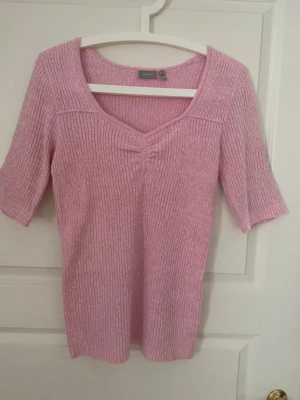 Rosa ribbad topp från Fransa - Söt ljusrosa ribbad topp från Fransa med v-ringad hals och halvlånga ärmar. Toppen är figurnära och har en mjuk, stretchig känsla som passar perfekt till jeans eller kjol. Enkel men ändå stylish design som är lätt att matcha.