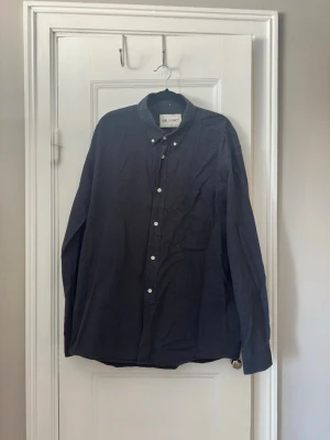 Mörkblå skjorta från Our Legacy | Storlek 54/XL - Klassisk mörkblå skjorta från Our Legacy med vit knappstängning och bröstficka. 100% bomull. I fint skick, sparsamt använd. 