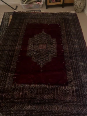 Mörkröd orientalisk matta med mönster - Säljer en stor, rektangulär orientalisk matta i mörkrött med detaljerade geometriska mönster i svart, vitt och grått. Mattan har en klassisk mittendel och breda bårder runt om. Perfekt för att ge rummet en mysig och unik vibe. Längd 250cm och bredd 160cm. Ordinarie pris 5000kr säljer för 2500kr. (Oanvänd)