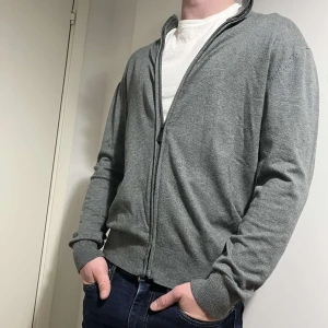 Grå kashmir kofta - Snygg och bekväm grå kofta med dragkedja framtill. Perfekt för lager-på-lager och passar till många olika stilar. Långärmad design med ribbade muddar för extra komfort. 40% kashmir.