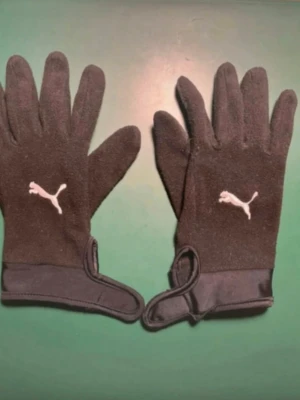 Puma Spelarhandskar Teamliga 21 - Svart/Vit - I mycket bra skick och knappt använda. Passar till alla typer av händer. Storlek M (långfingret till handled 22 cm). Nypris 299kr.  Mjuka handskar för kalla vinterlekar och träningar. Lätt akrylmaterial håller händerna varma och säkerställer en snäv passform. Silikon i fingrarna.