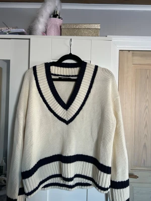 Vit stickad tröja från Gina Tricot - Vit stickad tröja från Gina Tricot med marinblå ränder och djup V-ringning. Aldrig använd men hann dra av lappen innan jag testade