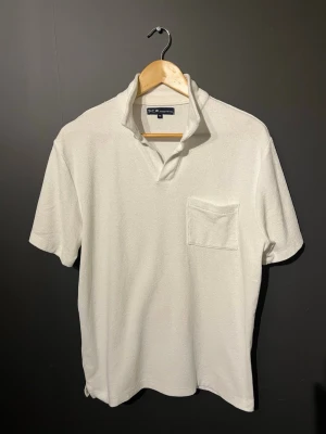 Vit frotté t-shirt från S.C.W - Vit t-shirt från S.C.W i mjuk frotté med klassisk krage och bröstficka. T-shirten har korta ärmar och en relaxed passform som ger en chill vibe. Perfekt för dig som gillar stilrena och bekväma plagg.