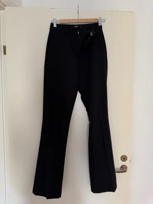 Svarta kostymbyxor från Gina Tricot - Snygga svarta kostymbyxor från Bik bok med raka ben och klassisk passform. Byxorna har hällor för skärp, dragkedja och knapp framtill. Perfekta för en stilren look och passar till många olika outfits.