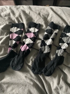 Argyle knästrumpor svart, grå & rosa - Två par ridstrumpor med klassiskt argylemönster i svart, grått, vitt och rosa. Perfekta för dig som vill ha en preppy look. Mjuka och stretchiga, troligen i bomullsmix. Säljs som ett set. Barn storlek 
