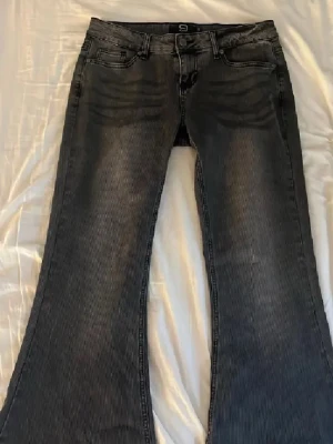 Grå bootcut jeans  - Säljer ett par grå bootcut jeans från R by EMP med klassisk femficksmodell och snygga slitningar framtill. Jeansen har en markerad utsvängd passform nedtill och är tillverkade i ett slitstarkt denimtyg. Perfekta för dig som gillar retrovibbar och vill sticka ut.