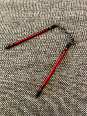 Nyckelring med röda mininunchakus - Unik nyckelring med två små nunchakus i metall, målade i rött och svart. Kedjan binder ihop de två stavarna och ger en cool accessoar med kampsportstema. Perfekt för dig som gillar annorlunda detaljer på dina nycklar eller väska.