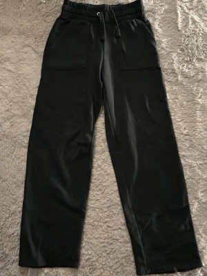 Svarta mjukisbyxor med raka ben - Säljer ett par svarta mjukisbyxor med raka ben och resår i midjan med dragsko. Byxorna har stora fickor fram och bak, vilket ger en avslappnad och trendig look. Perfekta för chill dagar eller när du vill vara bekväm men ändå se snygg ut. Dom är medel i midjan men man kan enkelt vika dom så blir dom låga.