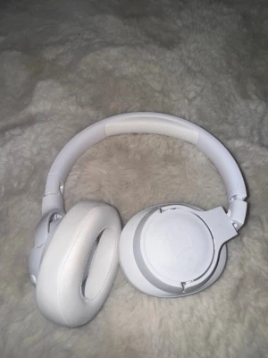 Vita JBL over-ear hörlurar - Snygga vita over-ear hörlurar från JBL med vadderad bygel och mjuka öronkuddar i konstläder. Hörlurarna har inbyggda knappar på sidan för enkel styrning och en stilren, modern design som passar perfekt till musik, gaming eller videos. Använda fåtal gånger. I nytt skick 