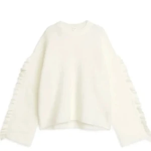 Vit stickad tröja med volangärm - Superfin trendig vit stickad tröja från Arket med volangdetaljer längs ärmarna. Tröjan har en rak passform, rund halsringning och långa ärmar. Perfekt för att ge en söt touch till din outfit!