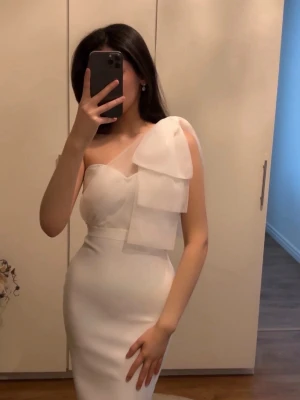 Vit asymmetrisk klänning med volang - PERFECT FÖR STUDENTEN! Säljer en elegant vit klänning med figurnära passform och asymmetrisk axel. Klänningen har en axel med transparent tyll och en stor volangdetalj som ger en unik look. Materialet är slätt och stretchigt, perfekt för dig som vill sticka ut. Klänningen slutar precis över knäna vilket inte syns på bilderna! 