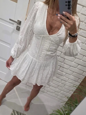  Ny  populär Vit broderad miniklänning från Zara med prislapp  - Söt vit miniklänning med broderade detaljer och v-ringning. Klänningen har långa puffärmar med resår vid ärmslut och en markerad midja som ger en feminin siluett. Tillverkad i ett lätt, luftigt tyg med hålmönster som ger en romantisk känsla.