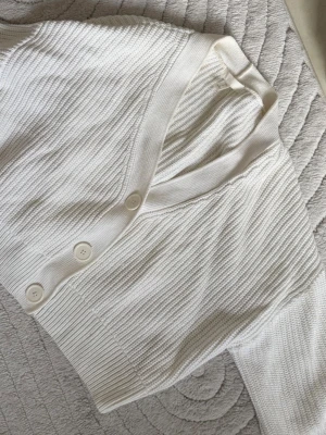 Vit ribbad kofta  - Säljer en vit ribbad kofta med stora knappar framtill och v-ringad hals. Perfekt för en sen sommarkväll 