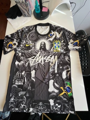 Stüssy x Brasil fotbollströja – Vini Jr på ryggen – Unik streetwear jersey - Säljer en sjukt snygg och unik fotbollströja från Stüssy inspirerad av Brasiliens herrlandslag i fotboll. Tröjan har cool svart/vit grafik med Brasil-detaljer och Nike Dri-FIT material som är lätt och bekvämt. På baksidan finns Vinícius Júnior, vilket gör den extra fet för fotboll & streetwear fans. • Skick: Mycket bra • Material: Dri-FIT (sportmaterial) • Passar perfekt till streetwear / fotboll / sommarfits • Sällsynt design – sticker ut 🔥 • Storlek: XS passar även i S stussy, brasilien, 