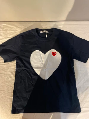 Svart t-shirt Comme des Garçons Play - Snygg svart t-shirt från Comme des Garçons Play med stort vitt hjärta och röd hjärtdetalj på bröstet. Klassisk passform och korta ärmar. Perfekt för dig som gillar streetwear och vill sticka ut lite extra.
