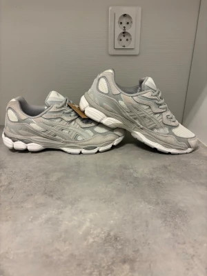 Gråa Asics sneakers mesh och mocka - Snygga sneakers från Asics i ljusgrått med detaljer i mesh och mocka. Skorna har en chunky vit sula och klassisk Asics-logga på sidan. Perfekta för dig som gillar sportig och clean stil. Lågt skaft och sköna att bära hela dagen.
