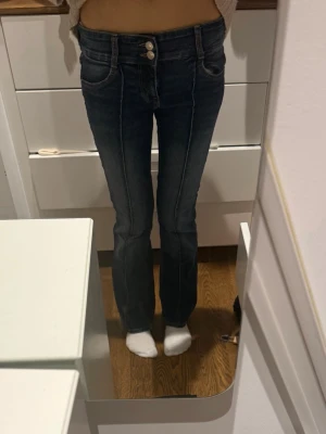 Blå bootcut jeans med dubbla knappar - Snygga blå bootcut jeans med dubbla knappar i midjan och markerade sömmar längs benen. Storlek 36