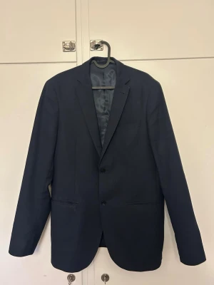 Marinblå Kostym - Snygg mörk kavaj med två knappar framtill och klassisk krage. Ingår även kostymbyxor till. 